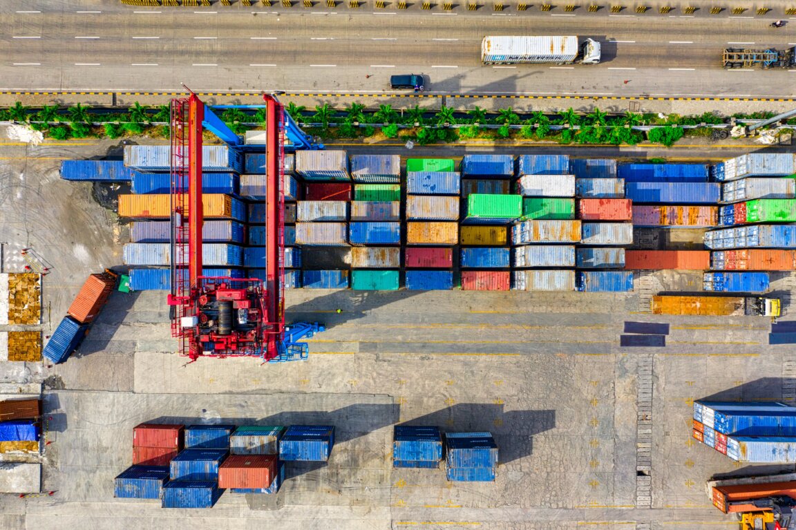 Aerial of colorful shipping containers beside three-lane freeway.