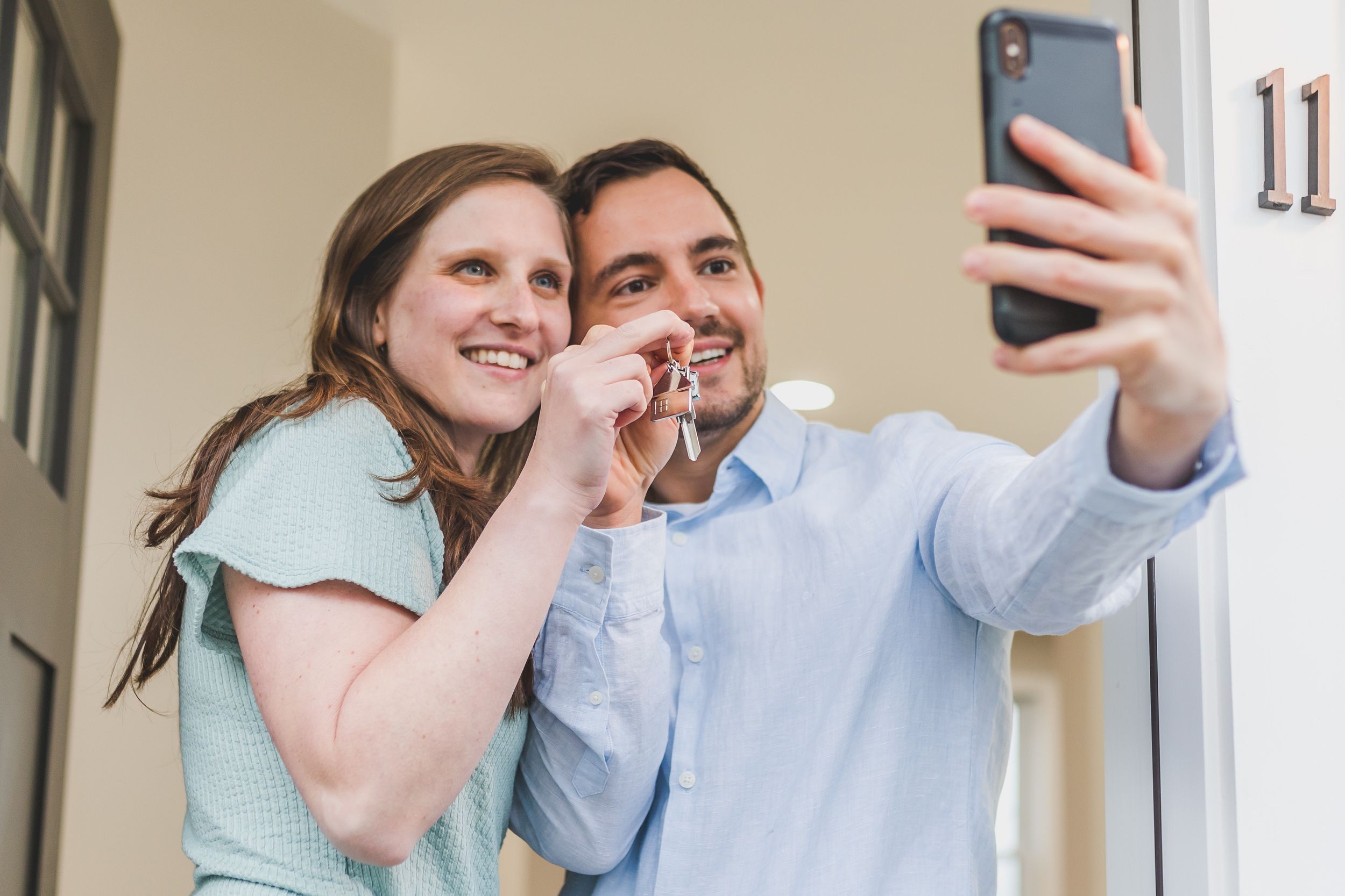 Young couple takes a selfie in front on a doorway while holding keys.