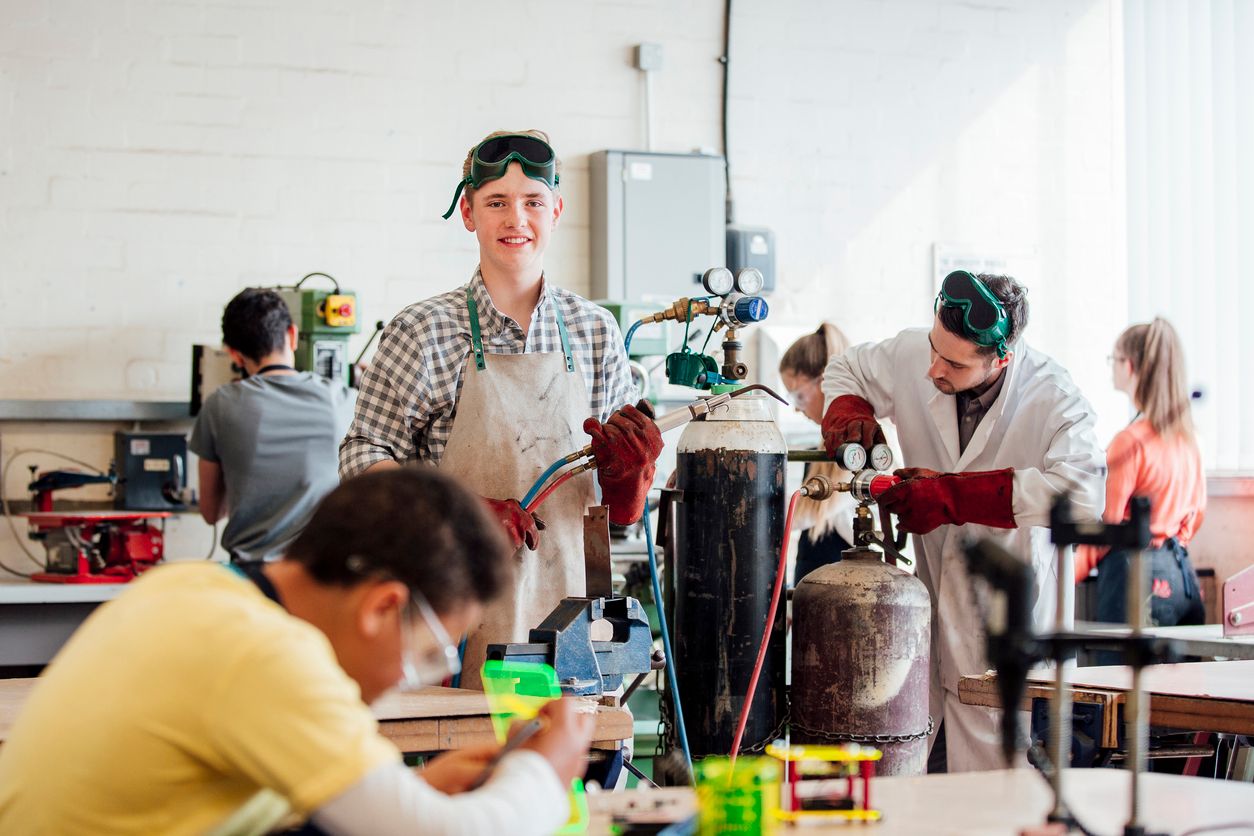 Male teenager practices welding in technical college class.