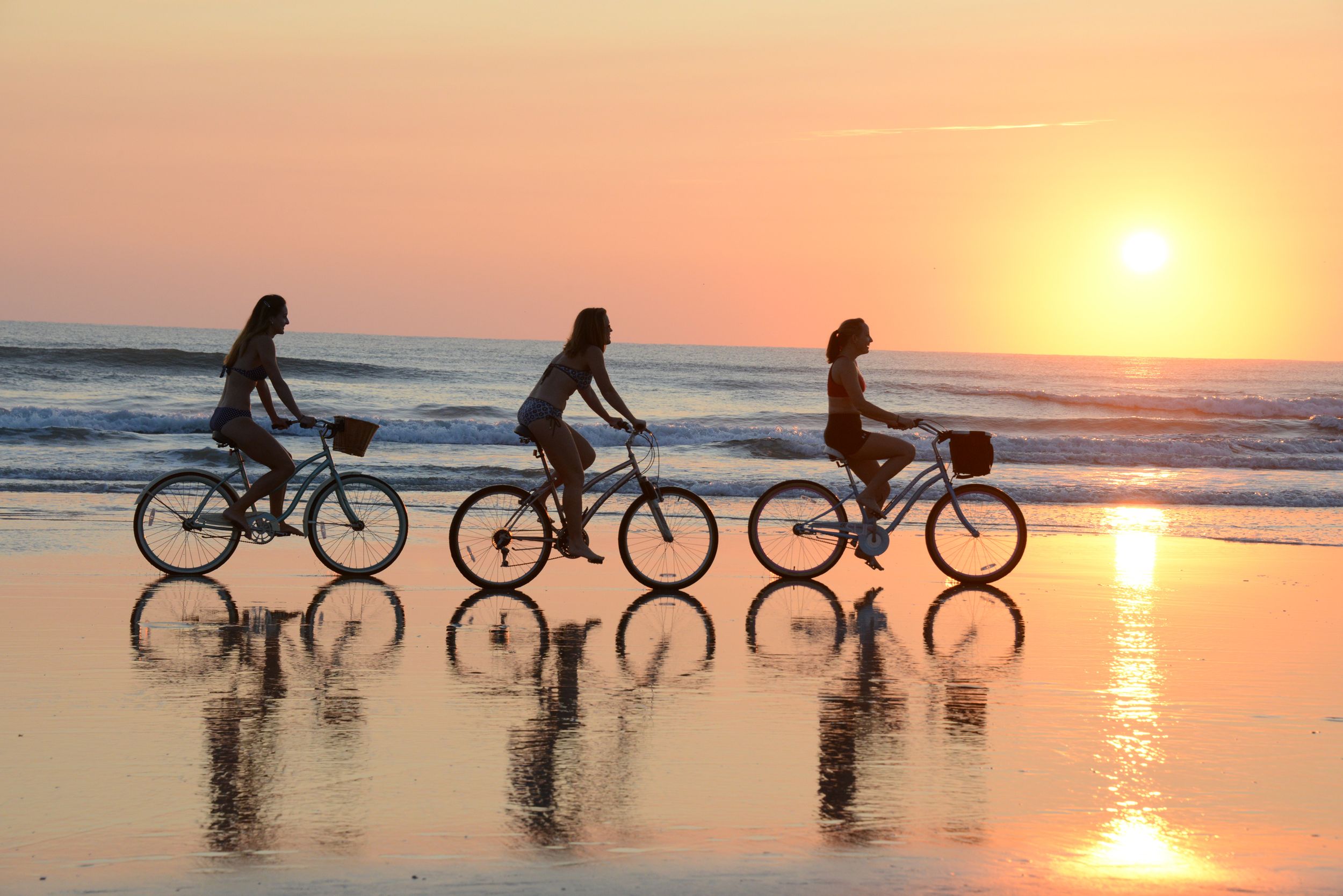 Three girls ride bicycles on the beach at sunrise